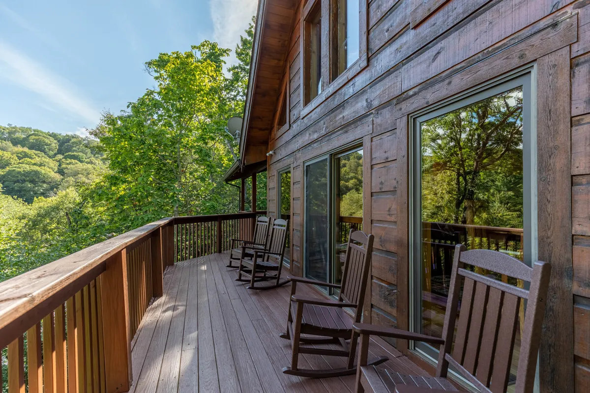 A welcoming shared deck with classic wooden rocking chairs overlooking natural surroundings. The wooden railing frames the view, suggesting a peaceful perch for watching sunsets or enjoying intimate conversations while immersed in mountain scenery.