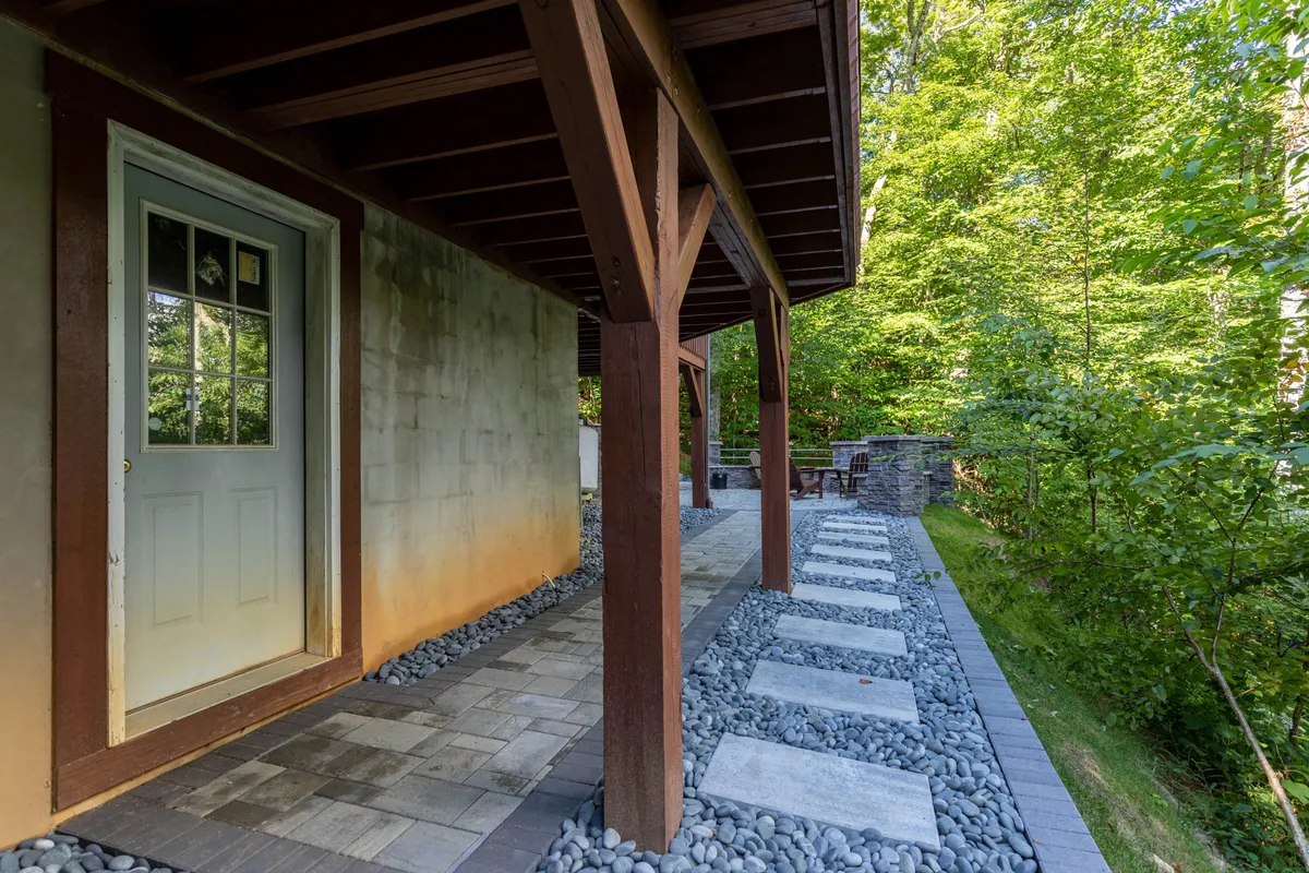 An inviting view of the cabin's doorway with a stone pathway, framed by lush greenery. The outdoor area suggests a welcoming entrance and a space suitable for pets and families to gather and enjoy the fresh air.