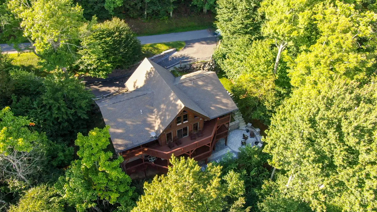 A serene view of a wooden cabin nestled among tall trees, featuring a spacious patio area and surrounded by natural greenery. The image evokes an inviting atmosphere for outdoor relaxation and exploration.
