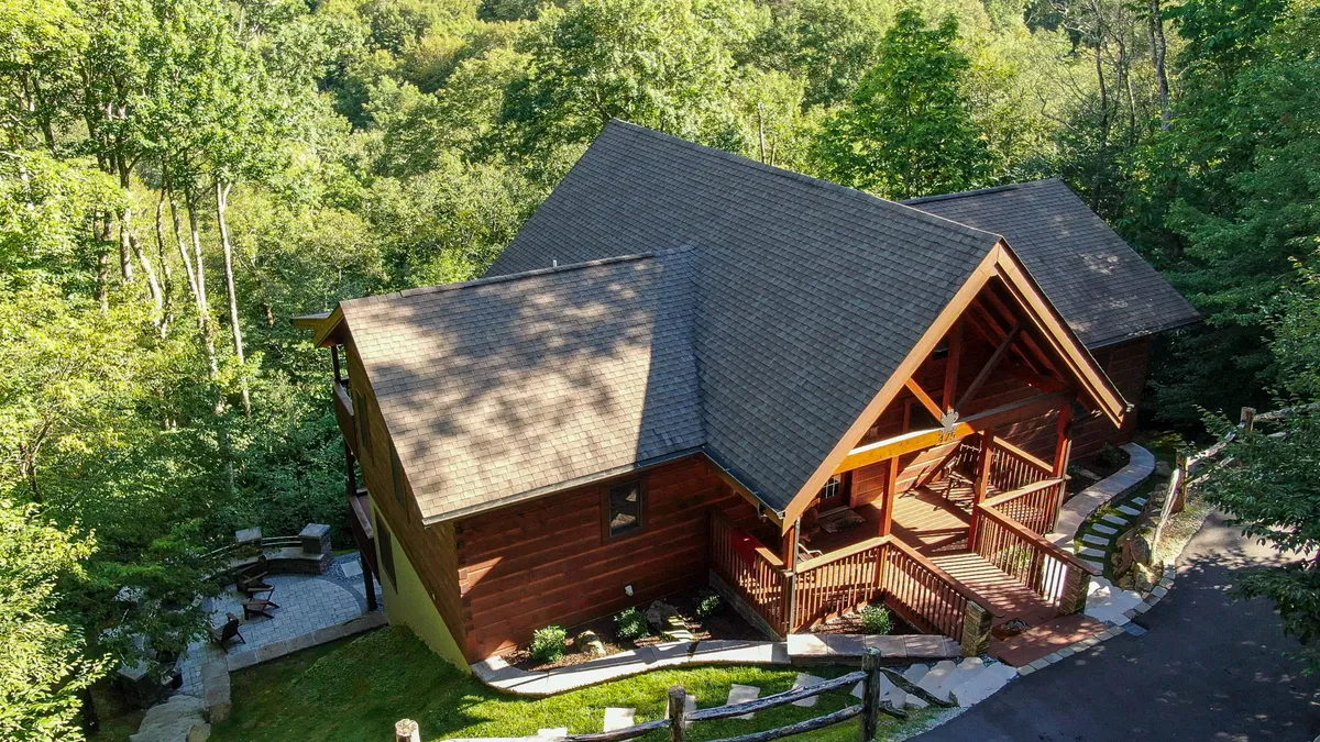 An expansive wooden deck with views of lush trees, a stone pathway leading into the natural surroundings, and space for relaxing or socializing. The atmosphere is tranquil, perfect for outdoor gatherings or enjoying a morning coffee while immersed in nature.