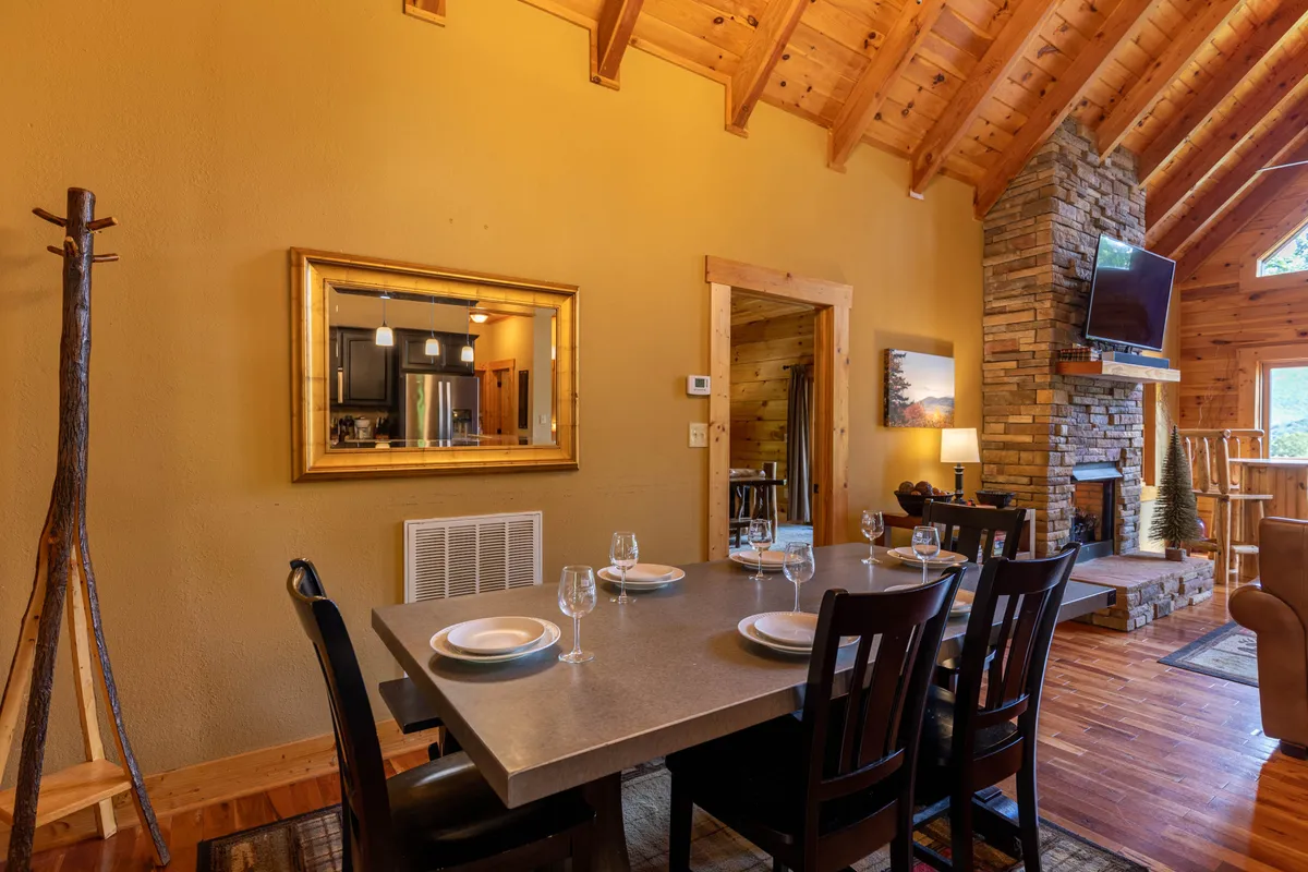 A welcoming dining area featuring a large table that seats eight, set beside a stone fireplace and expansive windows. The scene is filled with warmth and ready for family gatherings.