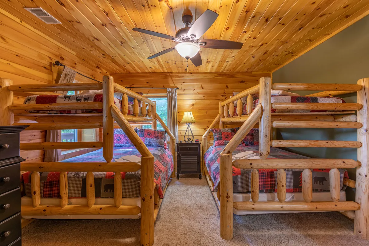 A cozy bunk room with wooden bunk beds, a warm ceiling, and a lamp on a nightstand. The atmosphere is playful yet snug, making it ideal for kids or teens seeking their own space.